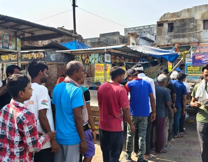 Men and boys stand close together in a crowd at a roadside stall under a tarpaulin.