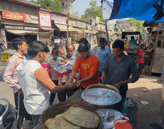 Volunteers serve from a large pot while a crowd, including an adult holding a small child, gathers around the counter.